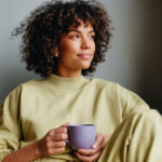 Woman holding a coffee mug by a sunlit window, symbolizing self-care for caregivers and intentional morning routine.