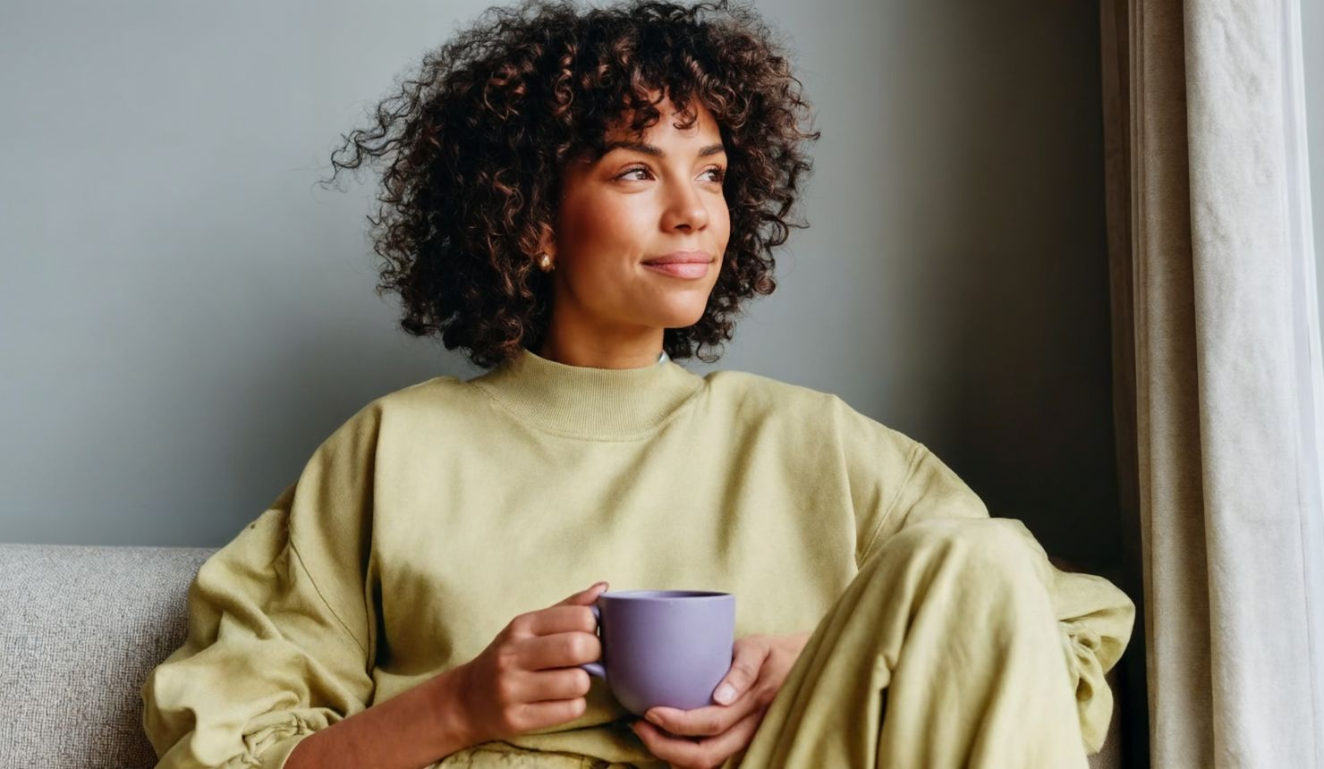 Woman holding a coffee mug by a sunlit window, symbolizing self-care for caregivers and intentional morning routine.