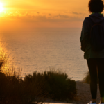 Person standing in an open field at sunrise, surrounded by expansive sky and soft morning light, symbolizing emotional clarity and inner reflection.