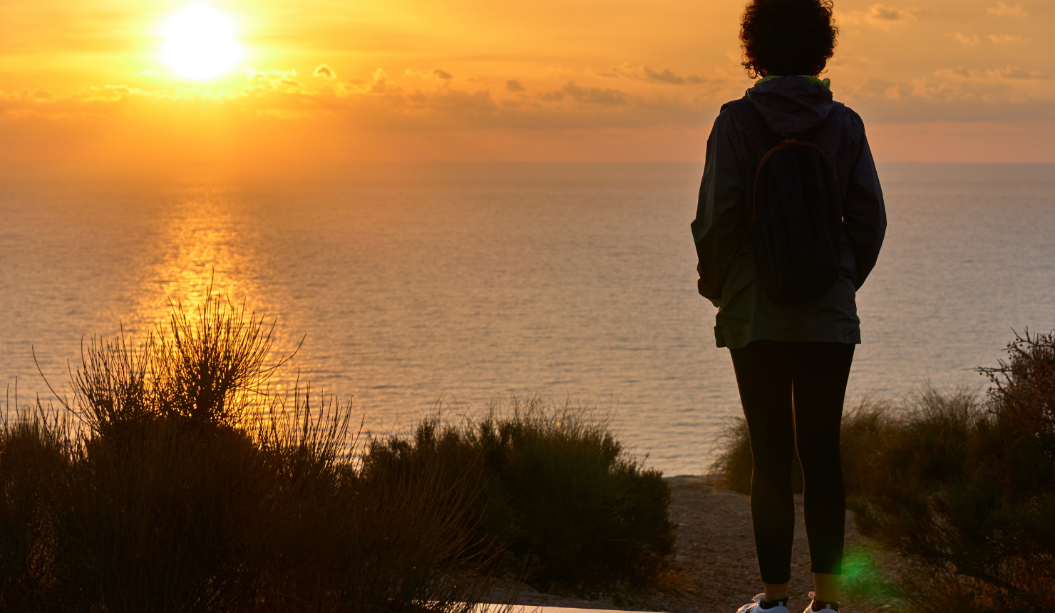 Person standing in an open field at sunrise, surrounded by expansive sky and soft morning light, symbolizing emotional clarity and inner reflection.