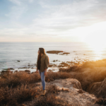 Woman reflecting peacefully by the ocean at golden hour, representing self-awareness, personal growth, and reconnecting with yourself through mindfulness and Reiki.