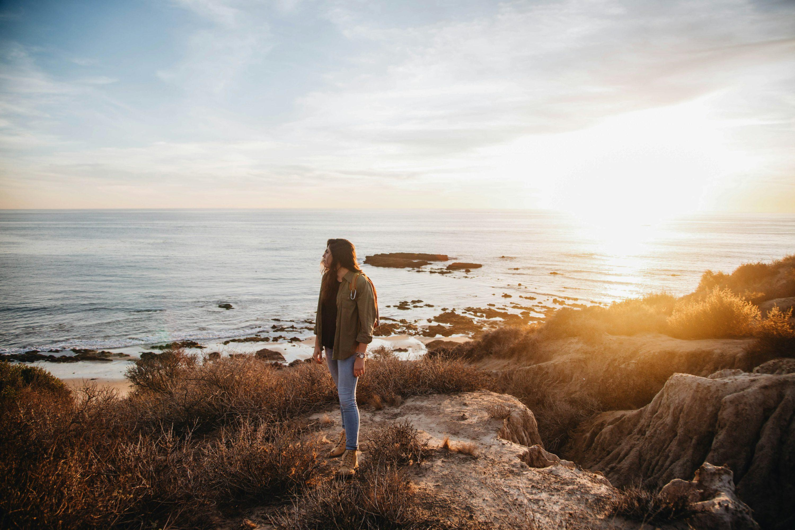 Woman reflecting peacefully by the ocean at golden hour, representing self-awareness, personal growth, and reconnecting with yourself through mindfulness and Reiki.