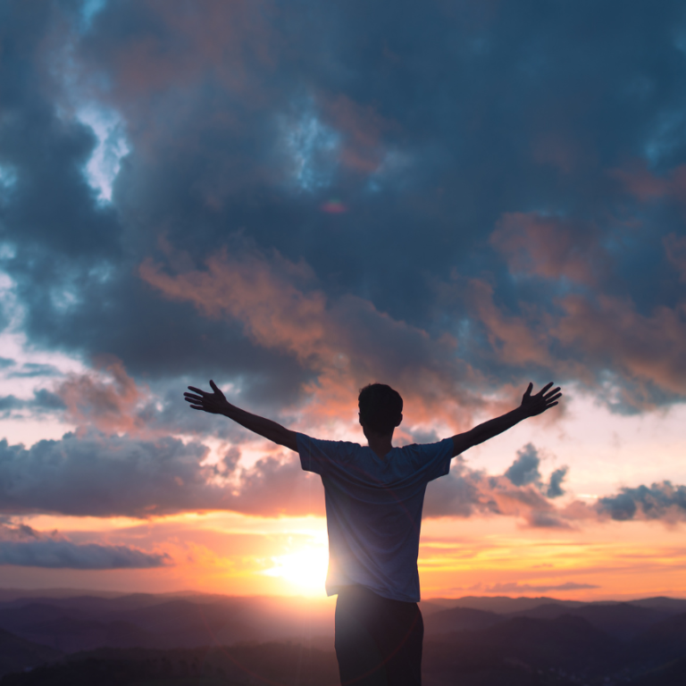 Man standing on a mountain at sunrise with arms outstretched, symbolizing freedom, openness, and gratitude